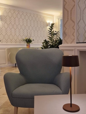 A modern living room with a grey armchair, a floor lamp, and a decorative vase with flowers. - Hotel Du Lac Gardone Riviera (Gardone Riviera)