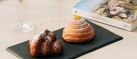 A table with a glass of orange juice, a pastry, and a book on a balcony overlooking a body of water.
