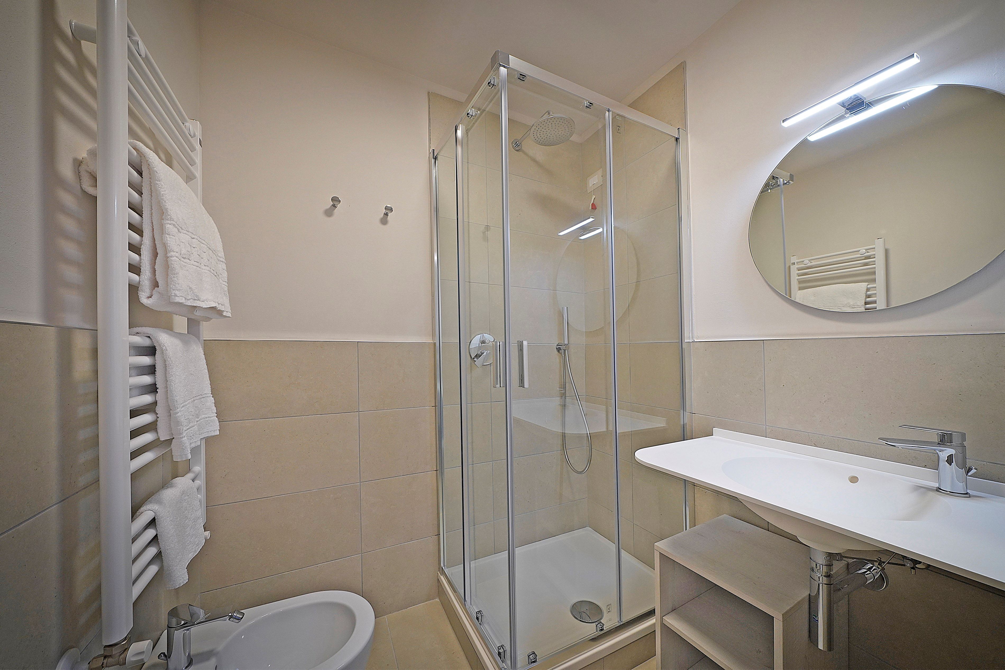 A modern bathroom with a glass-enclosed shower, a white sink, and a large mirror.