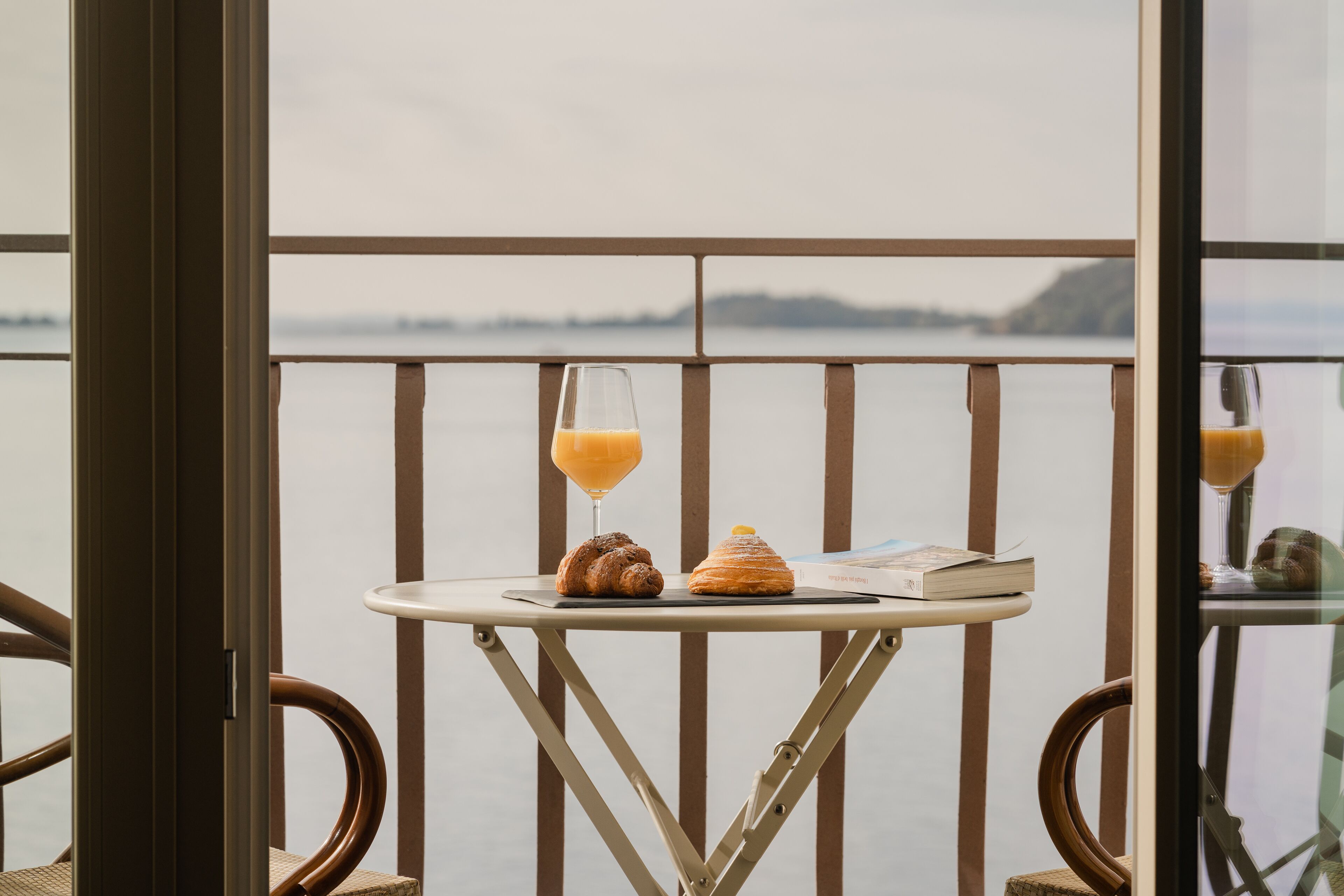 A balcony with a table set with a croissant, a glass of orange juice, and a book.