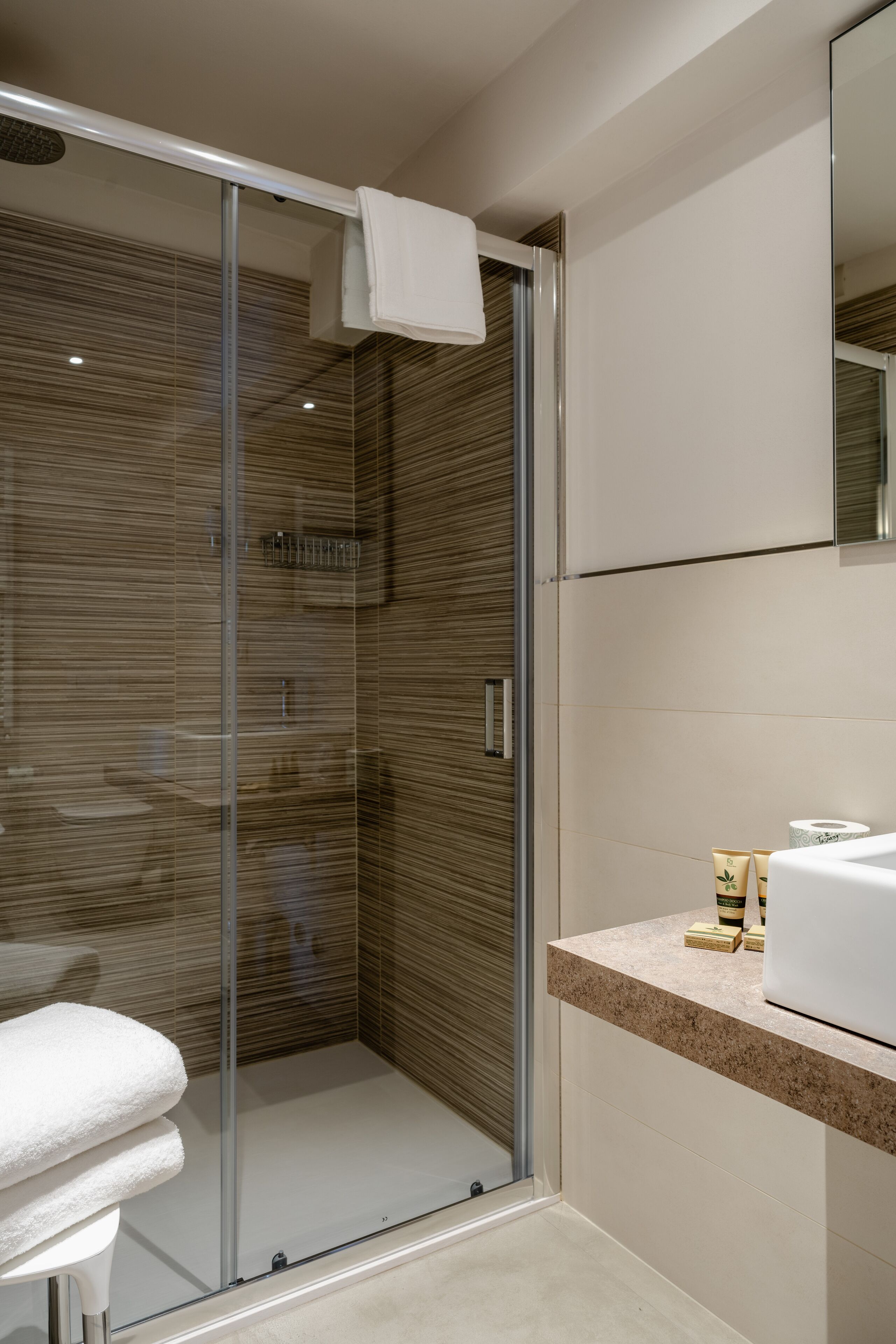 Een moderne badkamer met een douchecabine van glas, een witte wastafel en een spiegel erboven.