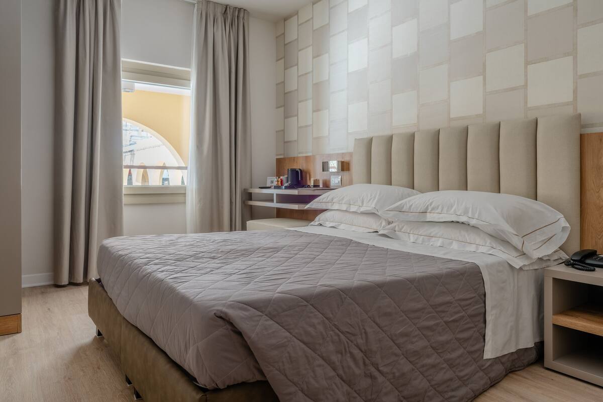 Une chambre d’hôtel moderne avec un grand lit, une table de chevet, un bureau et une fenêtre avec des rideaux.