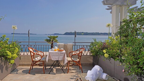 A terrace with two wicker chairs, a small table with a white tablecloth, and a towel on a mat. - Hotel Du Lac Gardone Riviera (Gardone Riviera)