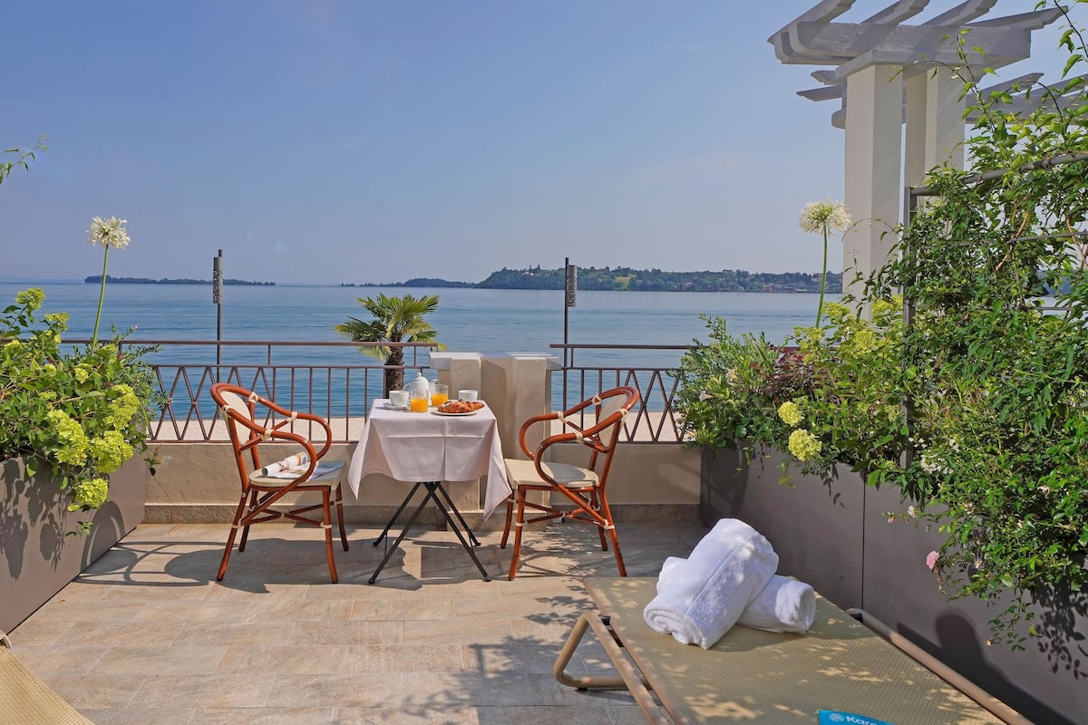 Une terrasse avec deux chaises en osier, une petite table recouverte d’une nappe blanche et une serviette posée sur un tapis.