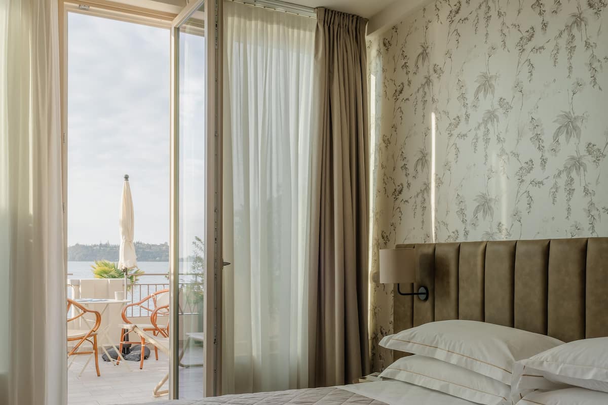 Une chambre d’hôtel avec un lit, un balcon doté d’une table et de chaises, et une vue sur la mer.