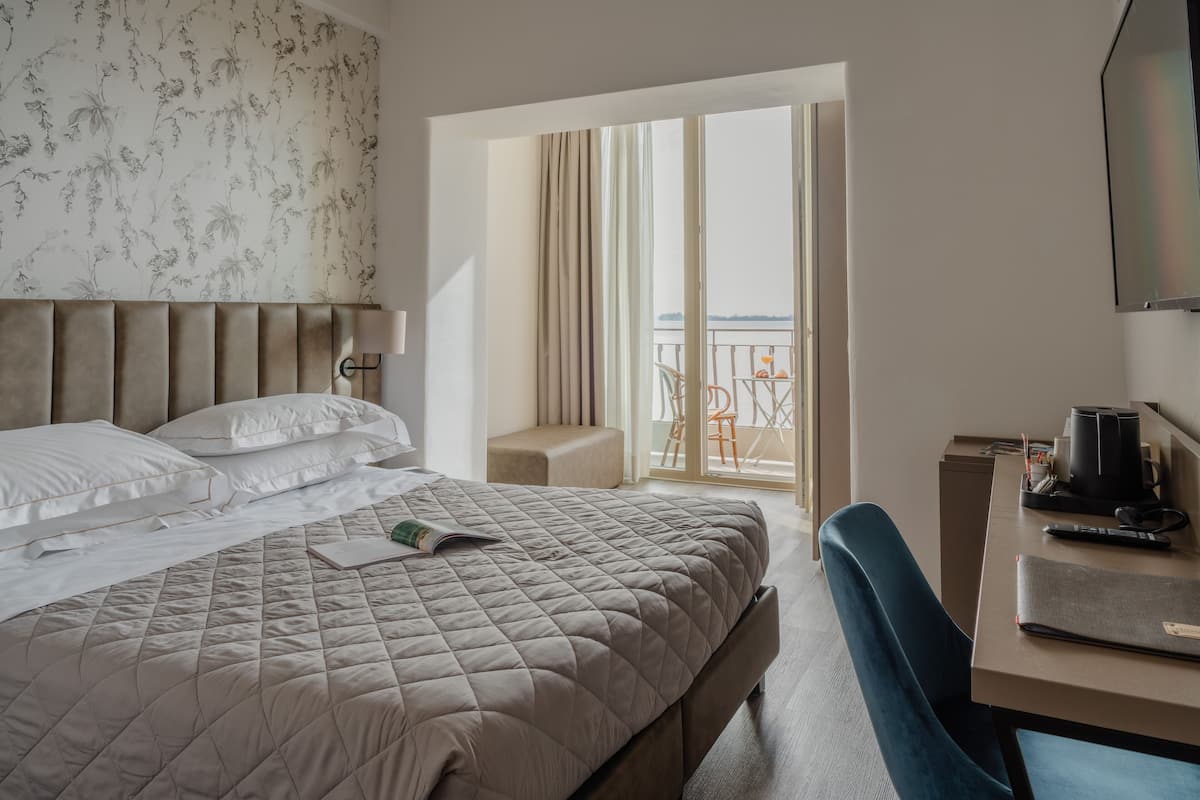 Une chambre d’hôtel avec un grand lit, un bureau avec un ordinateur portable et un balcon avec vue.