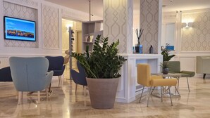 A modern lobby with a large potted plant, seating area with chairs, a TV mounted on the wall, and a patterned wall design. - Hotel Du Lac Gardone Riviera (Gardone Riviera)