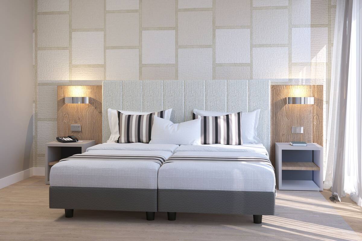 Un lit double avec une tête de lit rayée de gris et de blanc, deux tables de chevet avec des lampes et un mur à motifs en arrière-plan.