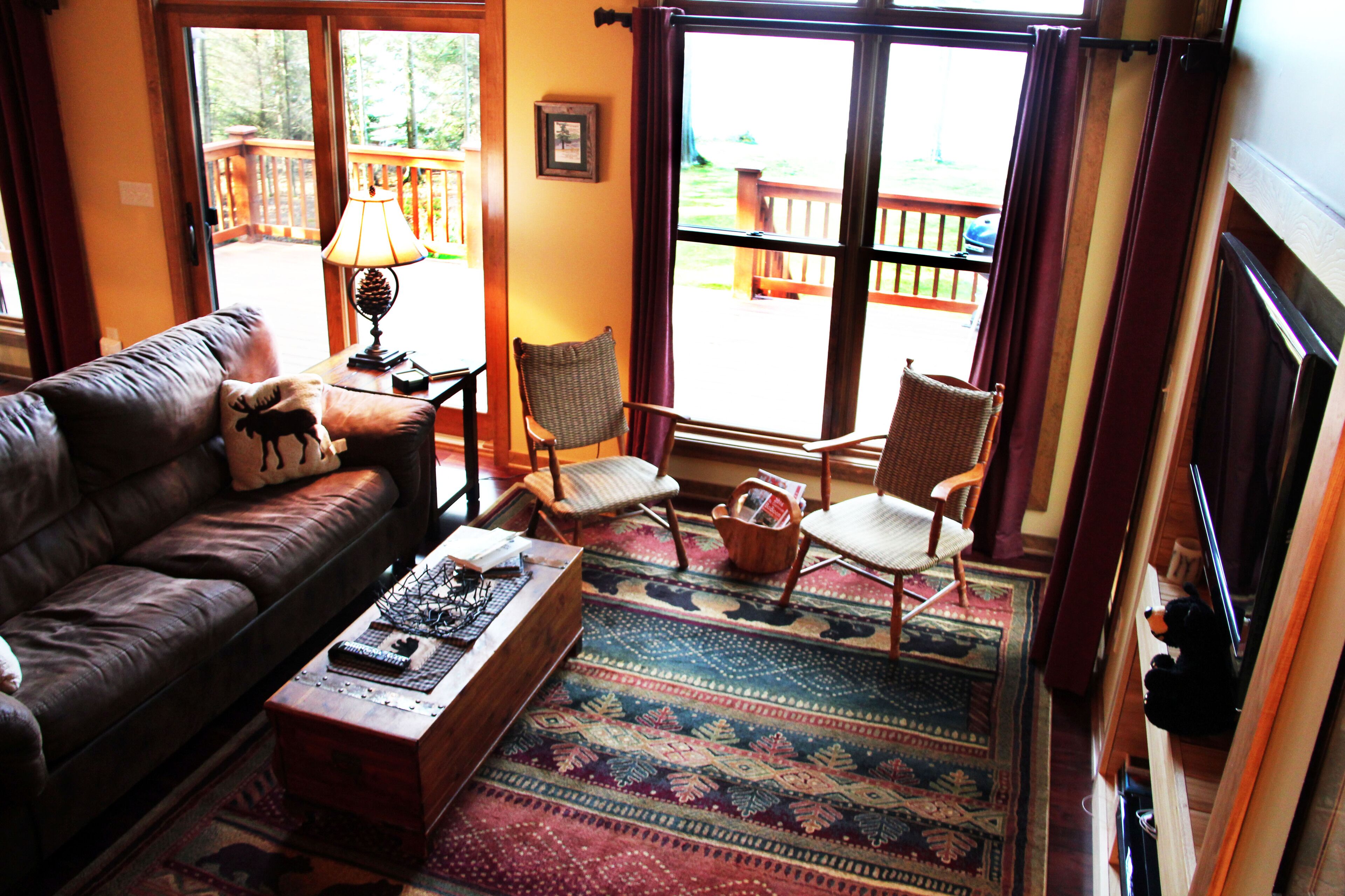 A cozy living room with a leather sofa, a wooden coffee table, and a patterned rug. There are two wicker chairs and a fireplace.