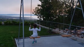A child on a swing overlooking a grassy area with a view of distant hills and a bridge. - "Nilaria" sea view apartment & pool near Krk, Rijeka (Bakar)