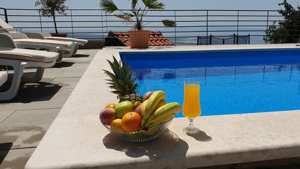 A poolside area with lounge chairs, a fruit bowl, and a glass of orange juice. - "Nilaria" sea view apartment & pool near Krk, Rijeka (Bakar)