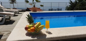 Ett område vid poolen med solstolar, en fruktskål och ett glas apelsinjuice.