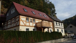 A traditional half-timbered house with a red roof, a wooden balcony, and a hedge in front.