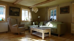 A cozy living room with a wooden floor, a green sofa, a beige armchair, a coffee table, and a painting on the wall.