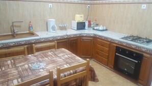 Een keuken met een houten tafel, stoelen, een spoelbak, een magnetron, een broodrooster, een gasfornuis en een vaatwasser.