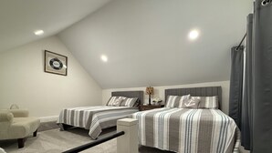 A bedroom with two beds, a chair, a nightstand, and a lamp.