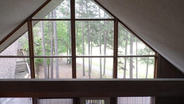 A room with a large triangular window offering a view of trees and a building outside.