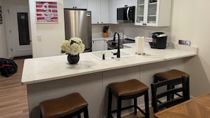 A modern kitchen with white cabinets, stainless steel appliances, a marble countertop, and a vase of flowers.