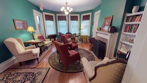 A traditional living room with a fireplace, multiple seating options, and a bookshelf.