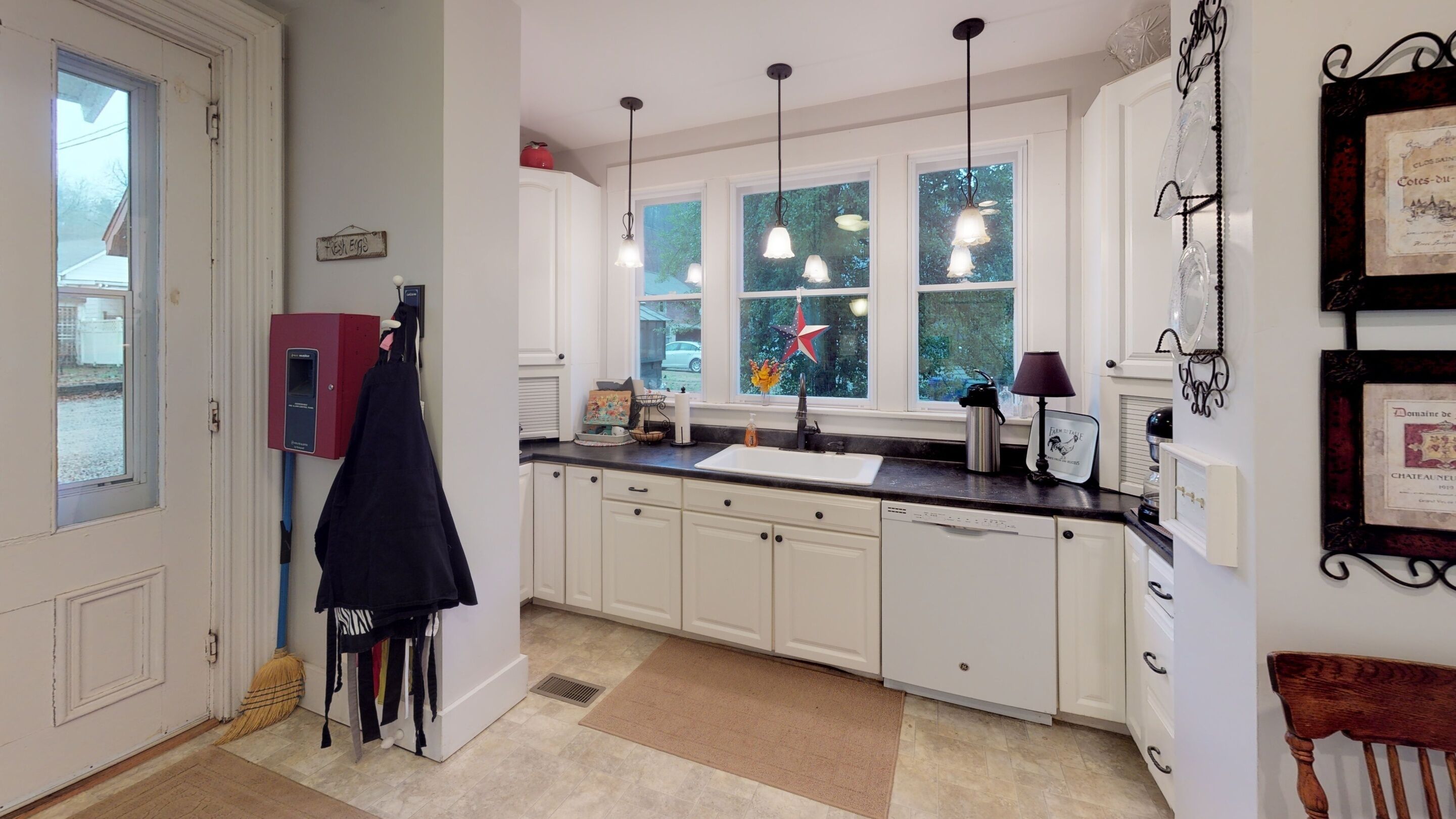 A kitchen with white cabinets, a black countertop, a window with a star decoration, and a red appliance.