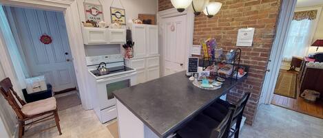 A kitchen with a central island, white cabinetry, a brick wall, and a door with a sign.