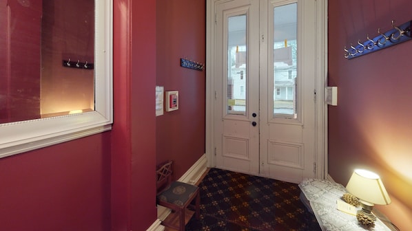 A hallway with a red wall, a white door with glass panels, a small wooden chair, a patterned rug, and a lamp on a side table.
