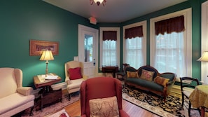 A room with teal walls, a red armchair, a green sofa, and a patterned rug.
