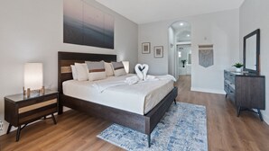 A modern bedroom with a large bed, bedside tables, a ceiling fan, and a view into another room.