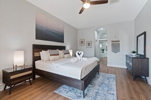 Quarto moderno com cama grande, mesas de cabeceira, ventilador de teto e vista para outro espaço.