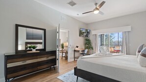 A bedroom with a large bed, a dresser, a desk, and a view of the outdoors.