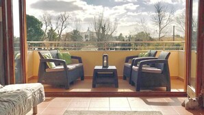 A balcony with wicker furniture, a small table, and a view of trees and buildings. - Licensed Beautiful large 2 Bed Apartment in Puerto Pollenca. 2 pools and balcony (Puerto de Pollenca)