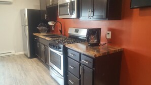 A compact kitchen with a gas stove, oven, and microwave. There are cabinets and a coffee maker.