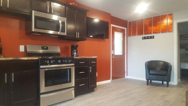 A modern kitchen with dark cabinetry, stainless steel appliances, and a flat-screen TV mounted above the oven.