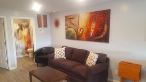 A living room with a brown sofa, two patterned pillows, a wooden coffee table, and a large abstract painting on the wall.