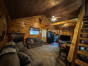 A cozy cabin interior with a fireplace, a sofa, a television, and a kitchen area.
