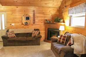 Ein gemütliches Blockhaus-Interieur mit zwei Sofas, einem Kamin und einem Spiegel an der Wand.