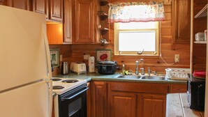 A wooden cabin-style kitchen with a refrigerator, stove, sink, and various kitchen items.
