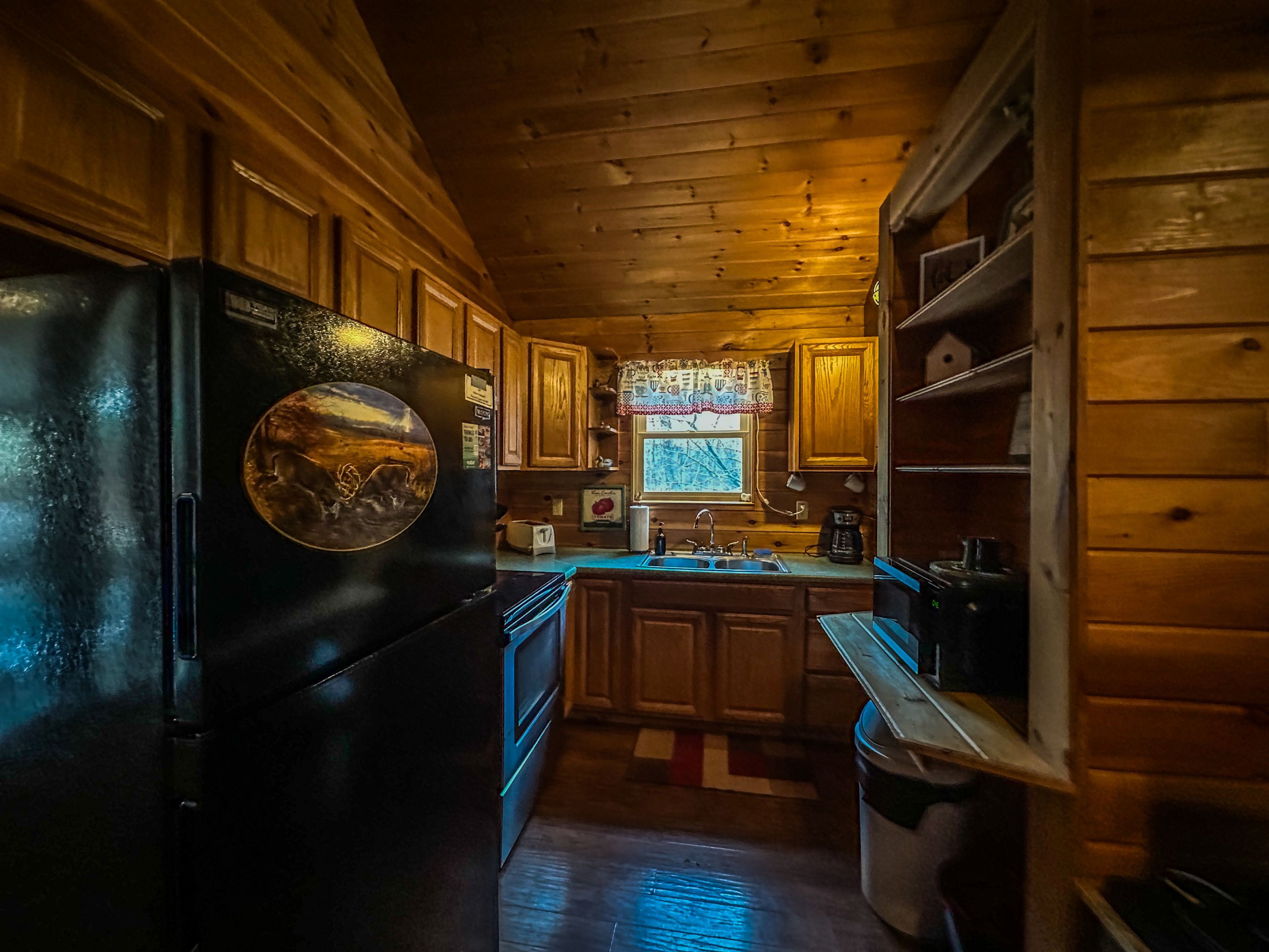 Une cuisine compacte avec des meubles en bois, un réfrigérateur noir et une fenêtre donnant sur un beau paysage.