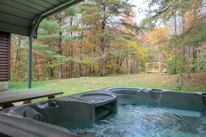 Ein Bereich mit Whirlpool, einer Holzterrasse und einem Picknicktisch, umgeben von einem Wald im Herbstlaub.