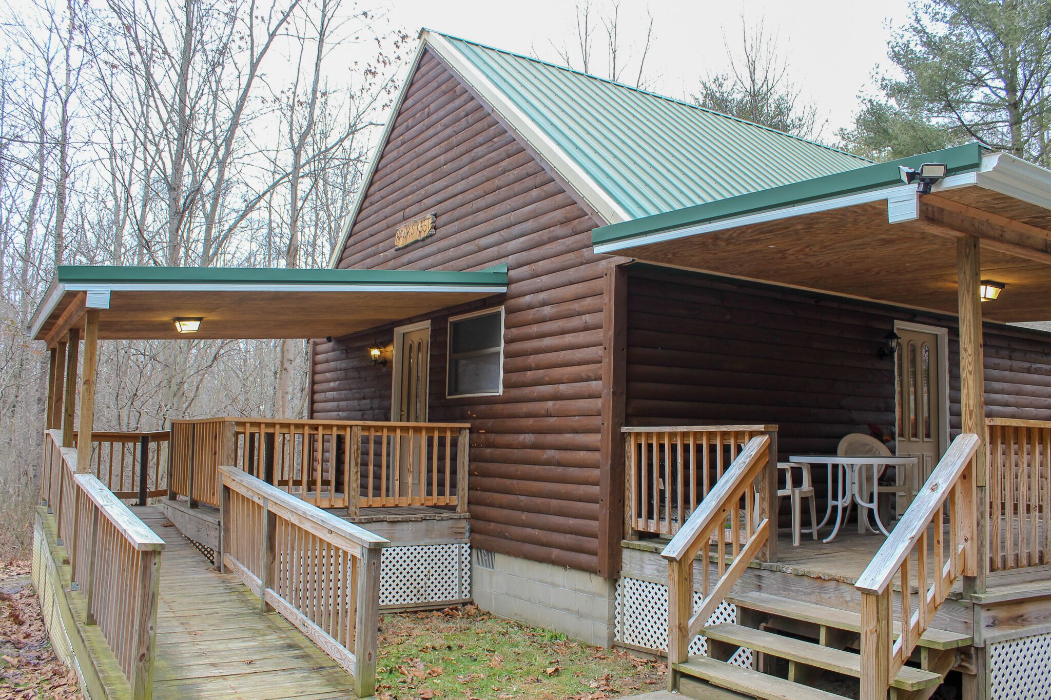 A wooden cabin with a covered porch, a deck, and a table and chairs set up outside.