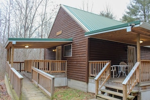 Eine Blockhütte mit Veranda und Deck, mit einem grünen Dach und Holzgeländern.