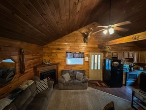 A cozy cabin interior with a fireplace, a sofa, a dining area, and a kitchen.