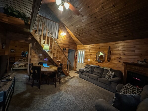 A cozy cabin interior with a dining area, a sofa, and a staircase leading to an upper level.
