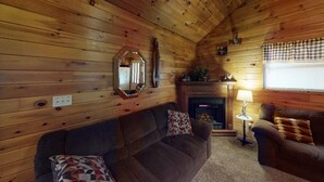 A cozy log cabin interior with a fireplace, wooden walls, a sofa, and a chair.