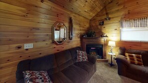 Ein gemütliches Blockhaus-Interieur mit Kamin, Holzwänden, einer Couch und einem Sessel.