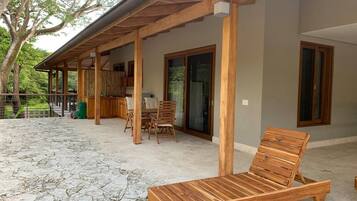 A covered outdoor area with a wooden lounge chair, a table, and chairs.