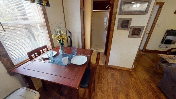 Un comedor con una mesa de madera, sillas y un jarrón con flores. Hay una puerta que da a un área de ducha.