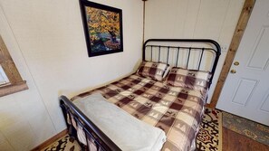 A single bed with a checkered bedspread and two pillows, a framed picture on the wall, and a door with a wooden frame.