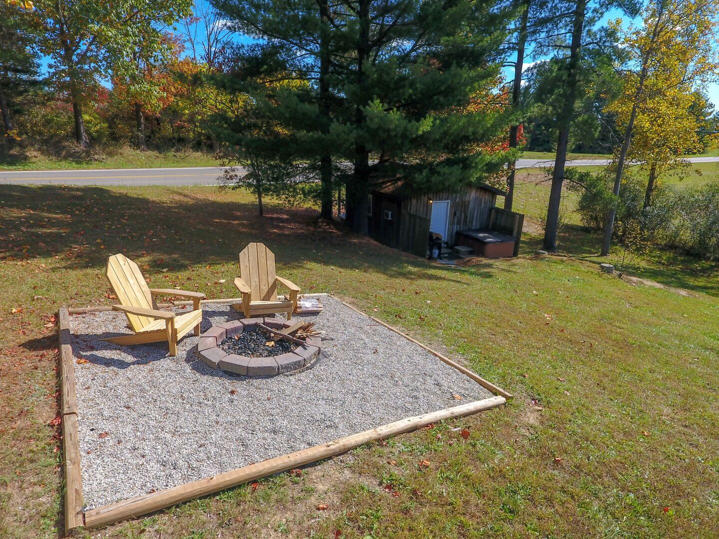 A fire pit area with two Adirondack chairs and a small shed in a grassy field.