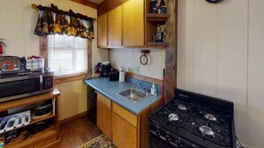 A compact kitchen with a microwave, stove, sink, and wooden cabinets.